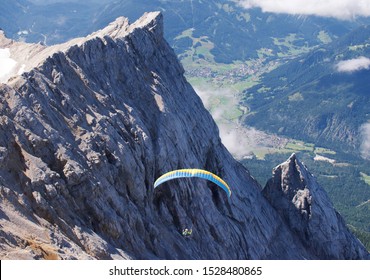 Person Paragliding From The Top Of Zugspitze Mountain With Jagged Cliffs In The Background