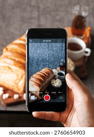 Person photographing a rustic bread setup with a smartphone on a dining table.