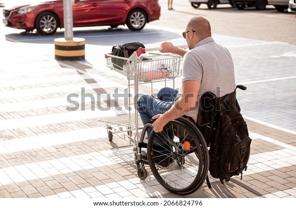 Person with a physical disability\
pushes a cart towards a car in a supermarket parking\
lot