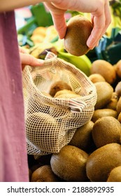 Person Picking Kiwi Fruit Into Reusable Knitted Eco Bag At Local Grocery Store