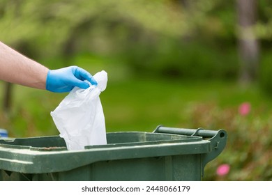 Person picks up a plastic bottle from the grass, holding a clear trash bag and collecting trash. the focus on environmental clean-up highlights a commitment to nature conservation. - Powered by Shutterstock