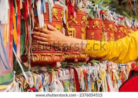 Person pilgrim female hand touching turning spinning Buddhist prayer wheel at Buddhist monastery. Prayer wheels in Buddhist stupa temple. Buddhism religion concept