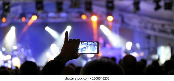 Person With The Pinky Hand Raised While Photographing The Rock Concert Using A Modern Smartphone