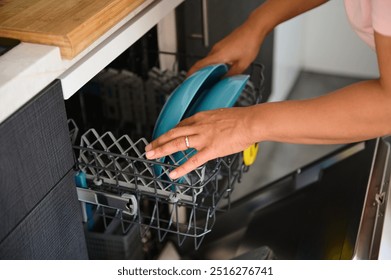 A person places blue plates in an open dishwasher, illustrating daily chores and kitchen organization. Focus on cleanliness and convenience in a modern home setting. - Powered by Shutterstock