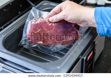 A person places a sirloin steak inside a vacuum sealed bag into a sous vide water bath to cook at 55C.
