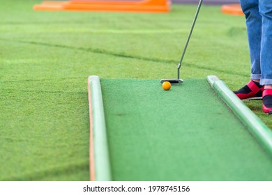 Person Playing A Game Of Miniature Golf On Artificial Green Turf In A Low Angle Cropped View Of Their Legs, The Ball And Golf Club With Copyspace