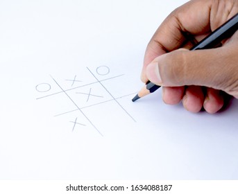 A Person Playing Tic Tac Toe On A Blank White Paper With A Black Wood Pencil In His Hand