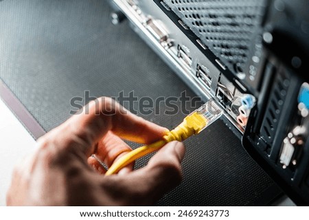 A person plugging a yellow Ethernet cable into the back of a computer. The image focuses on the hand holding the cable and the Ethernet port.