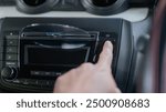 A person is pointing at the CD button in a car. The person is wearing glasses and is looking at the CD player