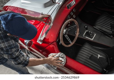 A person polishes the shiny surface of a vintage red sports car in a garage. Sunlight highlights the car's details, creating a warm atmosphere. - Powered by Shutterstock