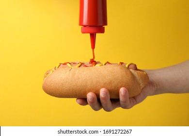 Person pouring ketchup on hot dog, on yellow background