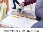 Person pouring maple syrup onto a bed of fresh snow to make a sweet maple taffy treat. Selective focus