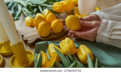 A person is preparing for Easter by arranging yellow dyed eggs and yellow tulips, with candles in yellow holders visible