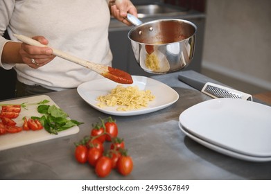 Person preparing pasta with tomato sauce in a kitchen, featuring fresh ingredients like tomatoes and basil on a cutting board. - Powered by Shutterstock