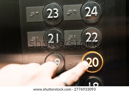 A person pressing the elevator button to the twenty floor of a modern elevator