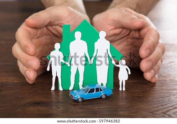 Person Protecting House Model With Family Paper Cut\
And Car On Wooden Desk