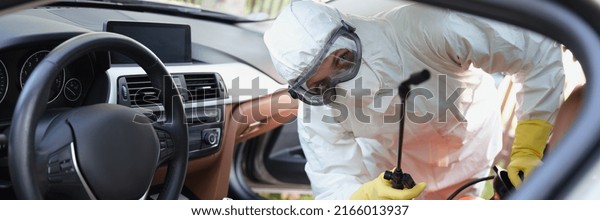 Person in protective costume clean surfaces in car\
with disinfectant spray