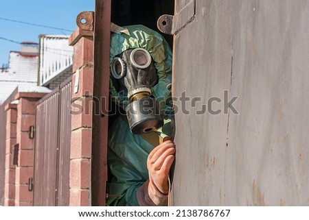 Person in protective suit looking through open iron gate door outside. Nuclear war danger and safety concept.