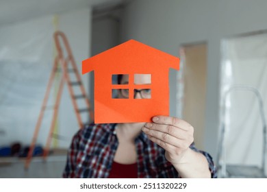 A person proudly holding an orange houseshaped cutout in their hands, symbolizing creativity in home renovation - Powered by Shutterstock