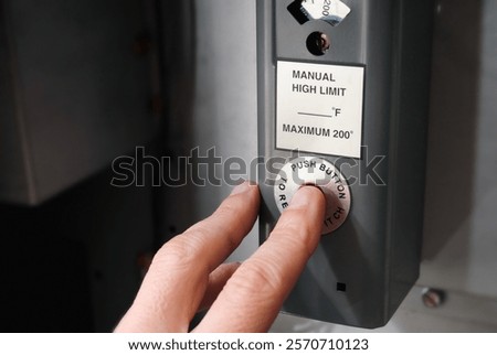 Person pushing reset button on hot water boiler. Natural gas boiler overheated or tripped. Female hand trying to restart the boiler. Hot water heating system or furnace background. Selective focus.