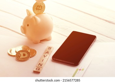 Person Putting Gold Bitcoin In Piggy Bank On A Desk And Others Bitcoins, Phone, Schedules And Title Saving How To Save More Money