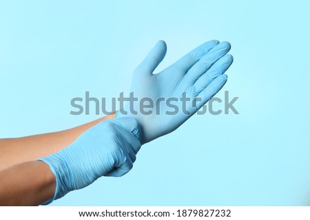Person putting on latex gloves against light blue background, closeup
