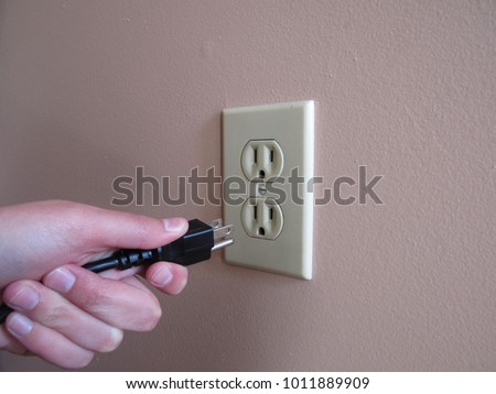 Person putting plug into American wall outlet 