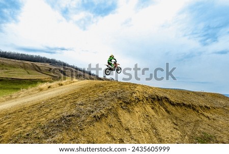 Person racing a motocross bike on dirt road under cloudy sky