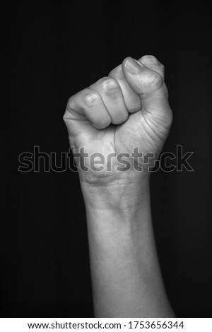 Person raised fist isolated on monochrome black background. The clenched fist, is a symbol of solidarity and support.Used as a salute to express unity, strength, defiance or resistance concept