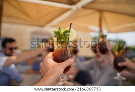 person raising and chinking with a long island ice tea cocktail.