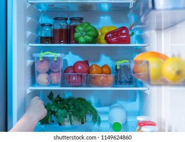 Person Reaching Inside A Fridge For Fresh Fruit And Vegetable Ingredients On The Shelves In A Close Up View Of Their Hand