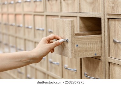 A person is reaching into a wooden drawer. The drawer is part of a large wooden cabinet. The cabinet is full of drawers and has a rustic, old-fashioned look - Powered by Shutterstock