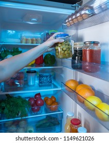 Person Reaching For Jar With Green Olives In Open Fridge Full Of Food