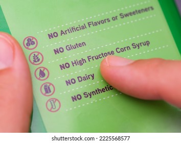 A Person Reading A Label With The Words No Artificial Flavors Or Sweeteners, No Gluten, No High Fructose Corn Syrup...