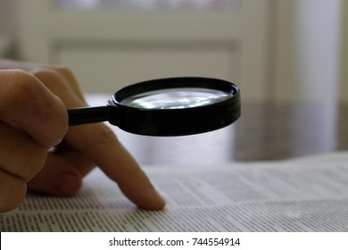 the person reads the document through a magnifying glass at the table