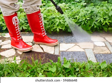 Person In Red  Gumboots Cleaning  Garden Alley With A Pressure Washer