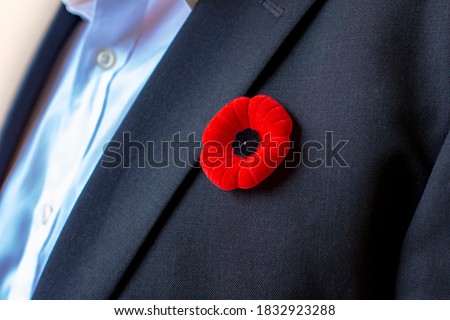 A Person with a remembrance day poppy flower on a black suit.