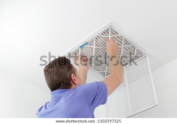 Person Removing Ceiling Air Filter. Caucasian male\
removing a square pleated dirty air filter with both hands from a\
ceiling duct. Guy taking out an unclean air filter from a home\
ceiling air vent