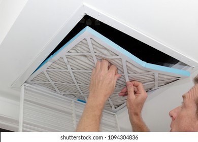 Person removing an old dirty air filter from a ceiling intake vent of a home HVAC system. Unclean gray square furnace air filter being taken out of a ceiling air vent.