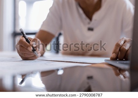 person reviewing documents and taking notes while using a laptop representing financial planning, business administration, record keeping, data management budgeting productivity.