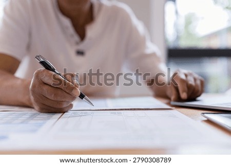 person reviewing documents and taking notes while using a laptop representing financial planning, business administration, record keeping, data management budgeting productivity.