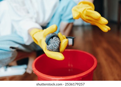 Person in rubber gloves holding a rock in a bucket, red bucket nearby, on wooden floor in hotel room - Powered by Shutterstock