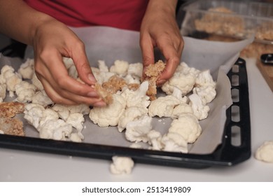 A person s hands preparing a baking tray with cauliflower florets and breaded chicken pieces, ready for the oven. Emphasizes the blend of fresh vegetables and protein for a balanced diet. - Powered by Shutterstock