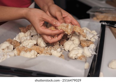 A person s hands preparing a baking tray with cauliflower florets and breaded chicken pieces, ready for the oven. Emphasizes the blend of fresh vegetables and protein for a balanced diet. - Powered by Shutterstock