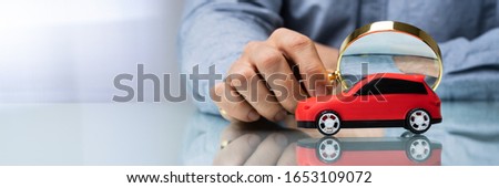 Person Scrutinizing A Car Model Using Magnifying Glass On Desk 