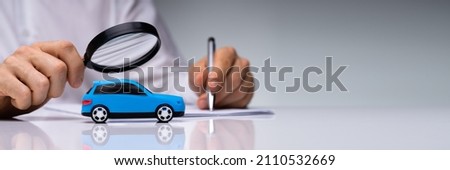 Person Scrutinizing A Car Model Using Magnifying Glass On Desk