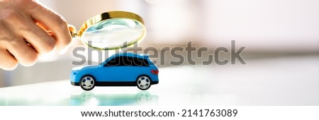 Person Scrutinizing A Car Model Using Magnifying Glass On Desk