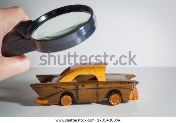 Person Scrutinizing A Wooden\
Car Model Using Magnifying Glass. Car search. Vehicle inspection\
with a magnifying glass. A man looks at a toy car with a magnifying\
glass.