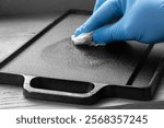 Person seasoning a cast iron plate with olive oil using a paper towel. On a wood background