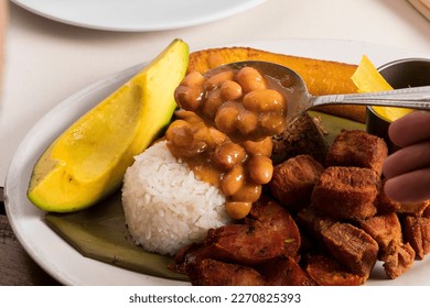 Person serving bean soup on the plate of additions of rice, avocado and fried pork, traditional Colombian lunch
